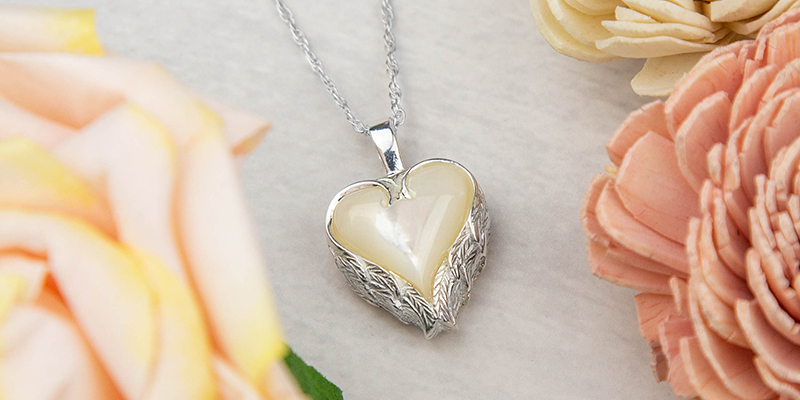 Stardust Memorials Heart Angel Wings Cremation Necklace posed between two pink roses.