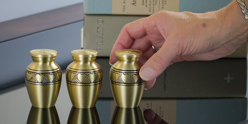 Three golden urns sitting on a table with a hand gently holding the right-most urn.